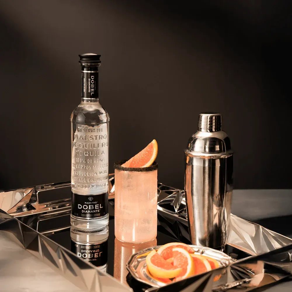 A bottle of vodka is sitting on a tray next to a glass and a shaker.