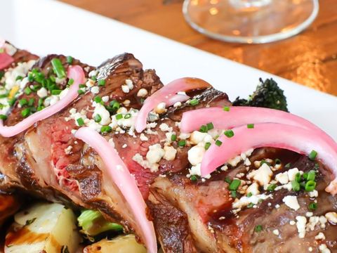 A close up of a plate of food with a glass of wine in the background