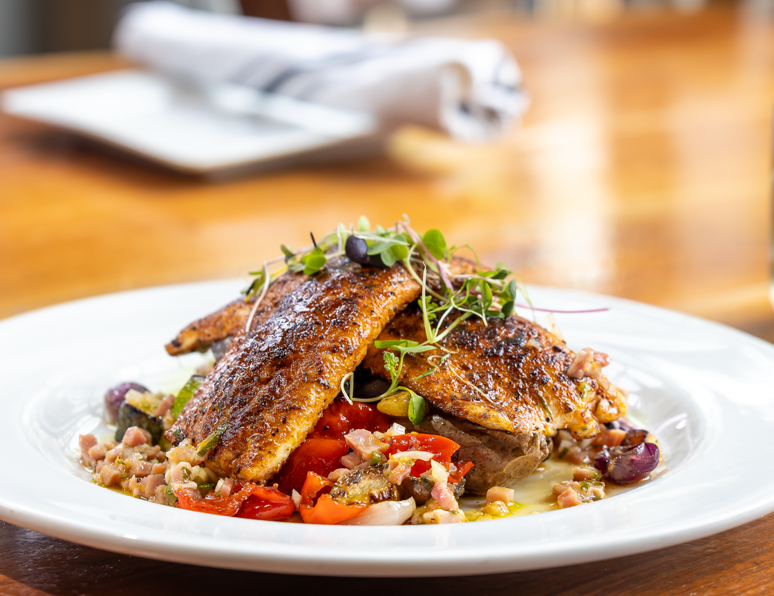 A close up of a plate of food with a glass of wine in the background