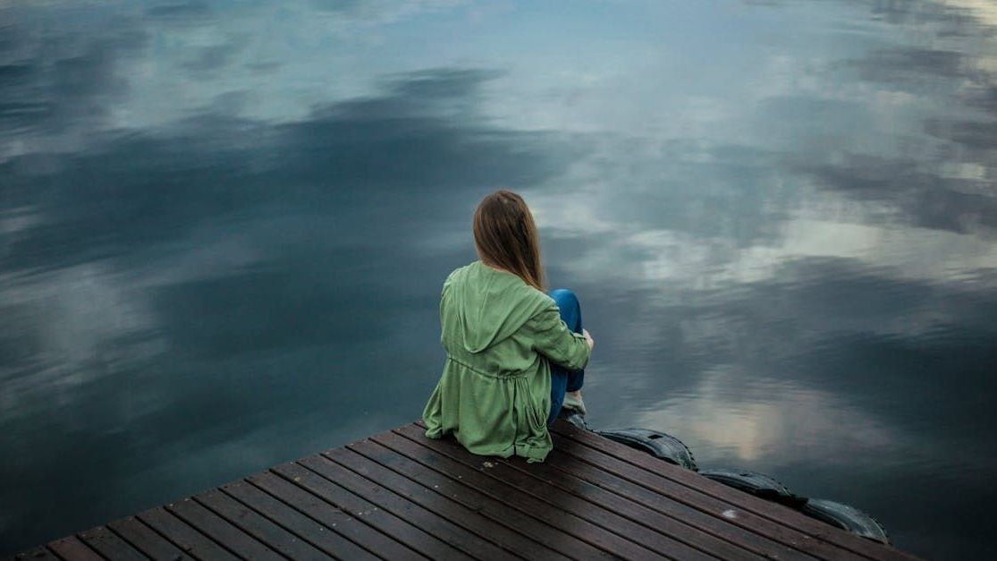 A woman is sitting on a dock looking at the water.