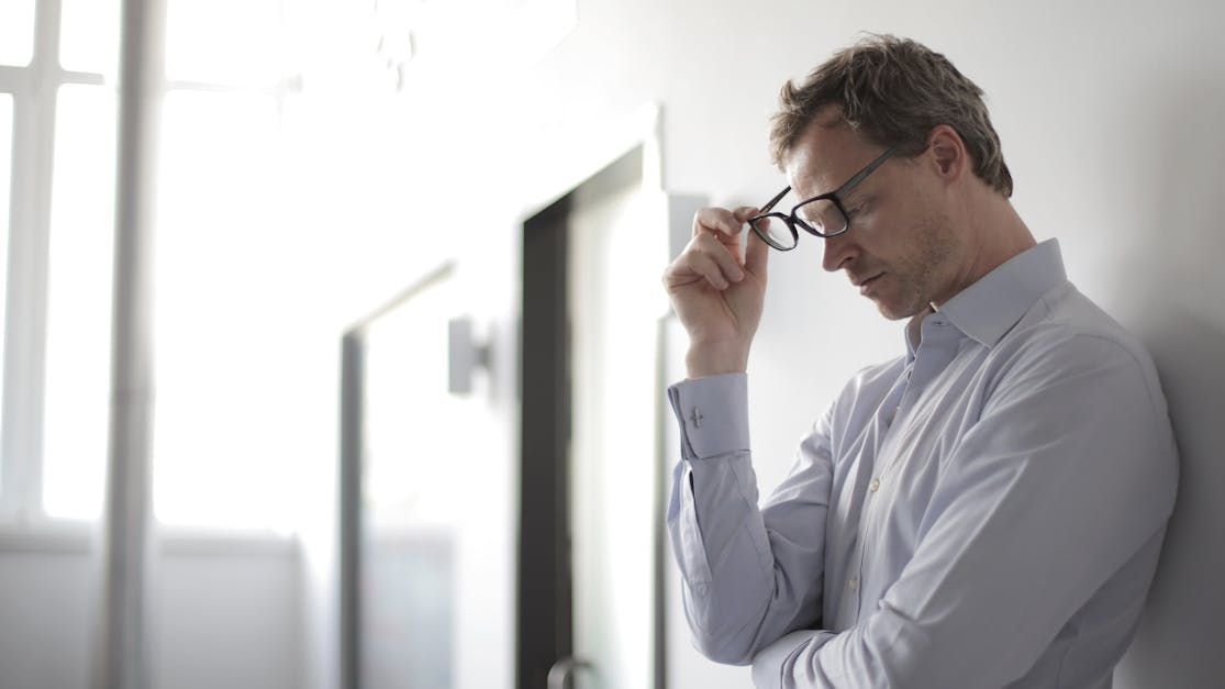 A man wearing glasses is leaning against a wall.