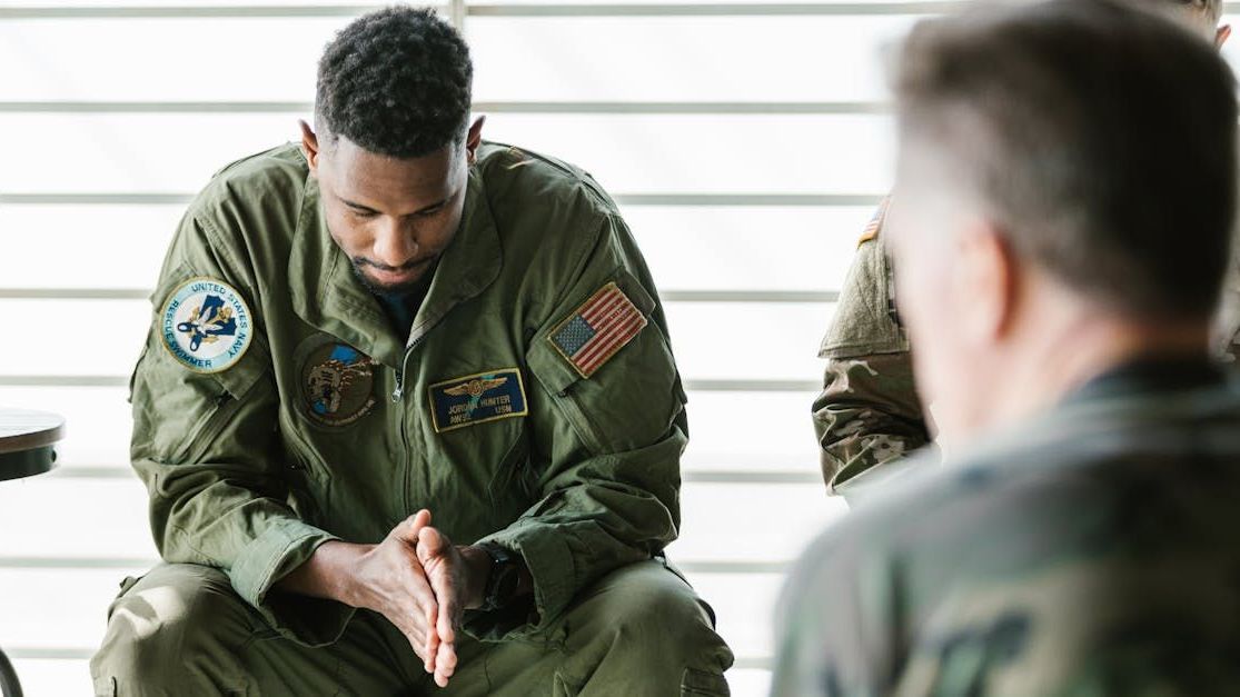 A man in a military uniform is sitting in a circle with other men.