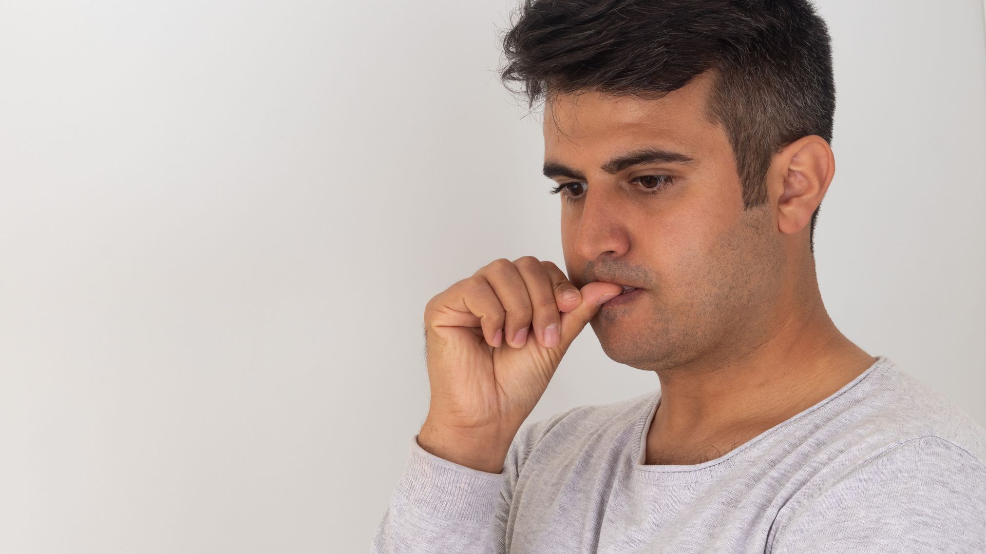 A man is biting his nails while looking down.