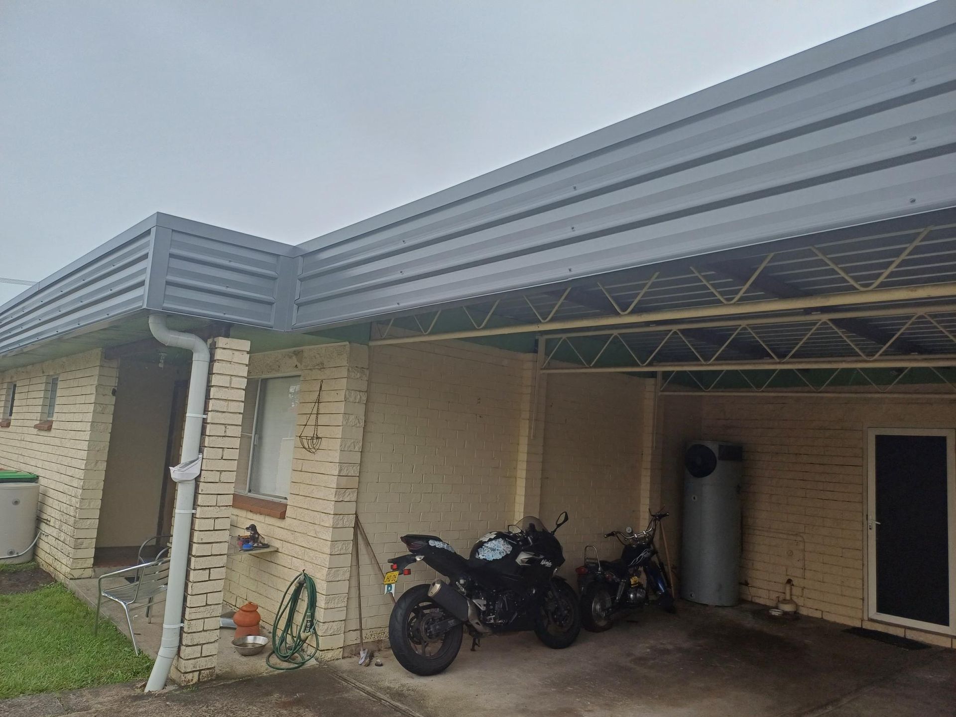 Two Motorcycles Are Parked Under A Carport On The Side Of A House — Rooftech Roofing Services in Yamba, NSW