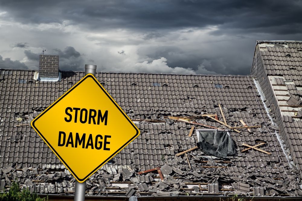 A Yellow Sign that Says `` Storm Damage '' Is in Front of A Damaged Roof — Rooftech Roofing Services in Ballina, NSW