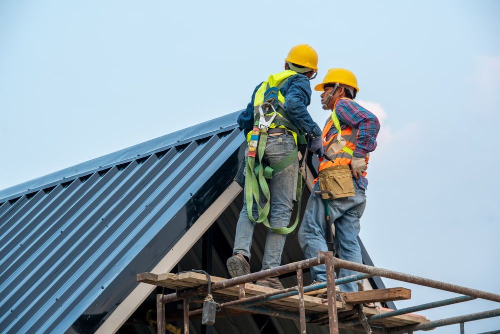 Two Construction Workers Are Standing on A Scaffolding on Top of A Roof — Rooftech Roofing Services in Byron Bay, NSW