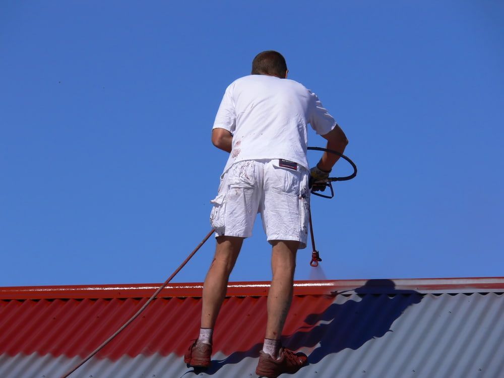A Man Paints a Red Roof with A Sprayer — Rooftech Roofing Services in Ballina, NSW