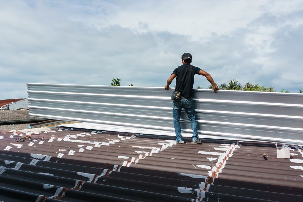 A Man Is Standing on Top of A Roof Holding a Piece of Metal — Rooftech Roofing Services in Byron Bay, NSW