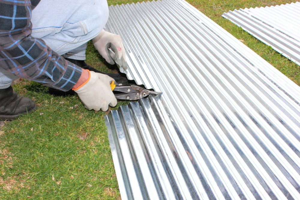 A Man Is Cutting a Piece of Corrugated Metal with A Pair of Scissors — Rooftech Roofing Services in Iluka, NSW