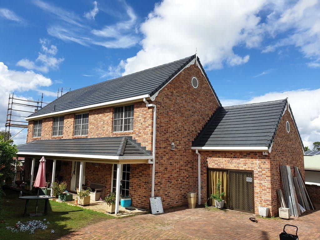 A Large Brick House with A Black Roof and A Garage — Rooftech Roofing Services in Yamba, NSW