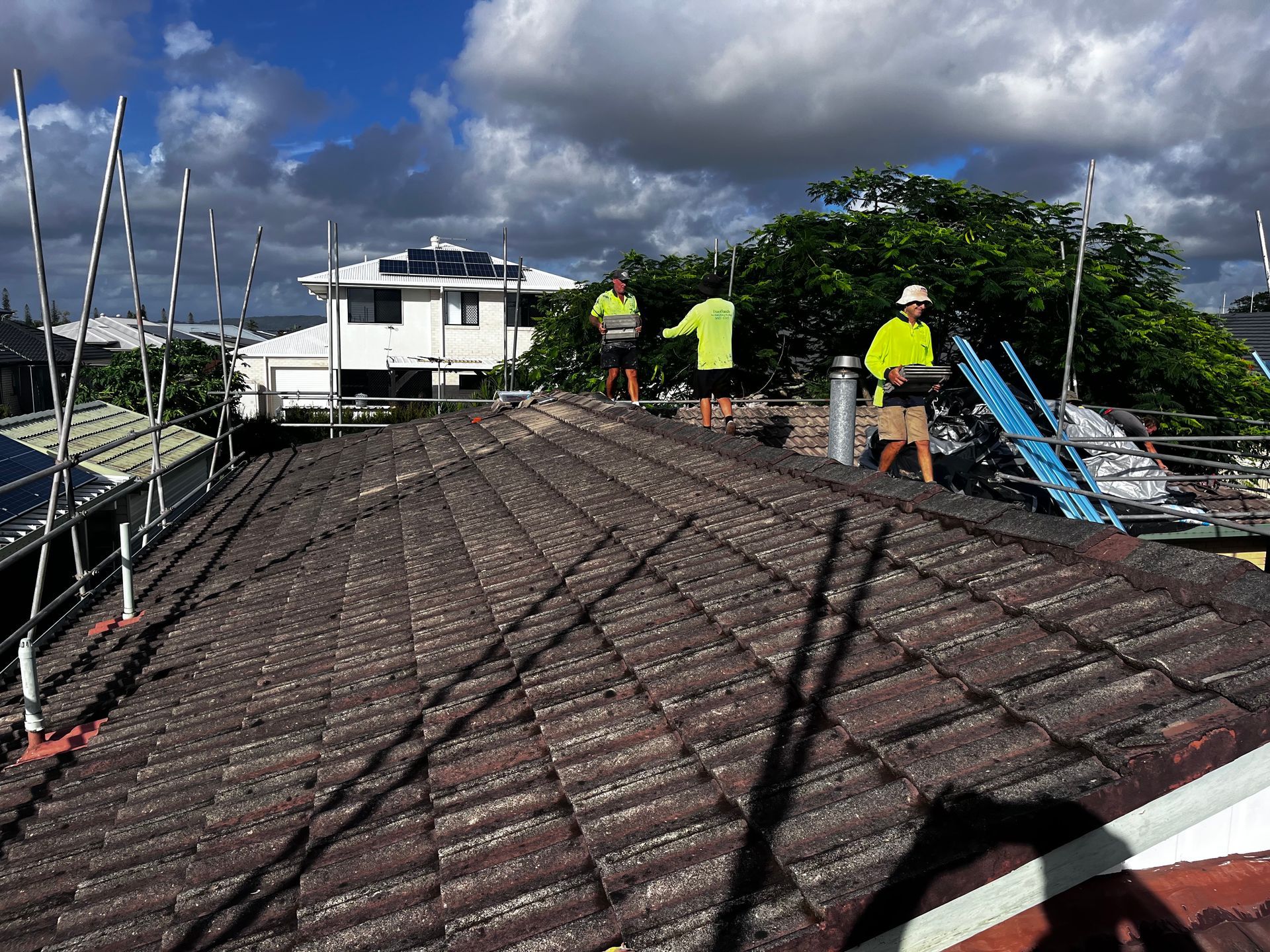 Three Men Working On A Tiled Roof With Scaffolding — Rooftech Roofing Services in Mullumbimby, NSW