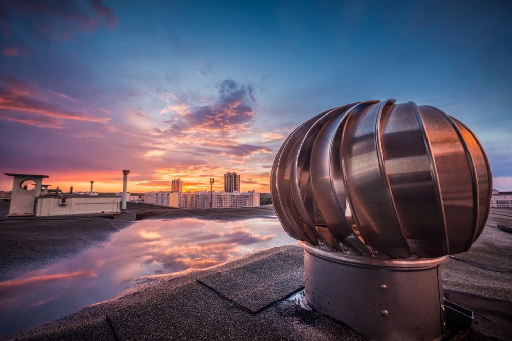 A Stainless Steel Exhaust Fan Is Sitting on Top of A Roof at Sunset — Rooftech Roofing Services in Yamba, NSW