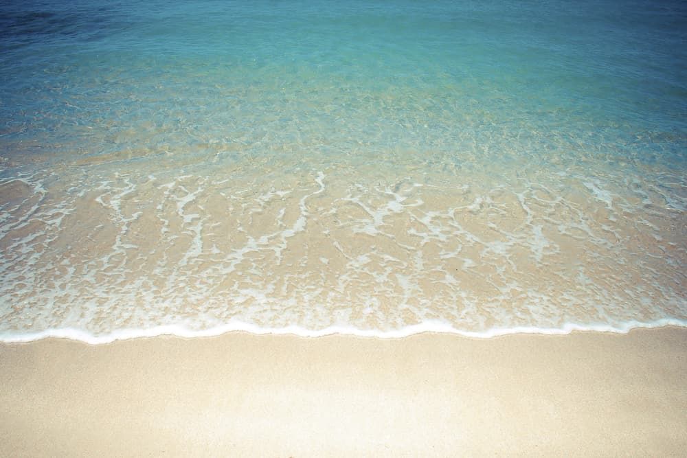 A Close up Of a Beach with Waves Crashing on The Sand — Rooftech Roofing Services in Ocean Shores, NSW