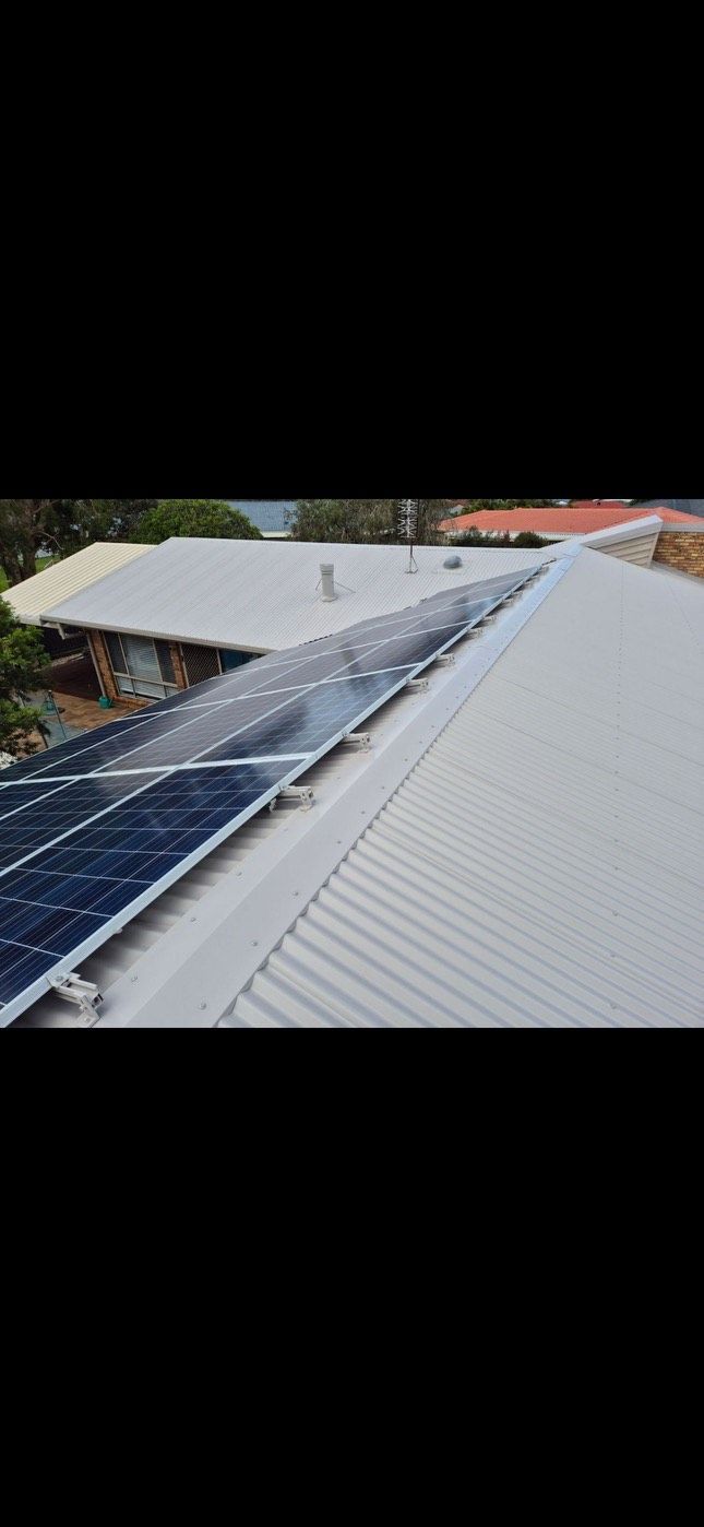 A Row Of Solar Panels Are Sitting On Top Of A White Roof — Rooftech Roofing Services in Ocean Shores, NSW