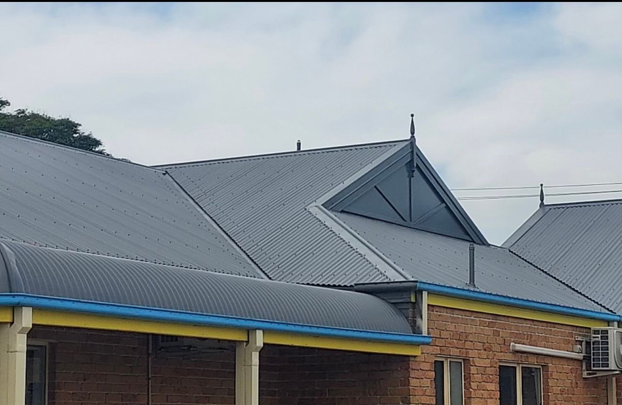 Gray Corrugated Metal Roof On A Brick Building With Blue Gutters, Against A Cloudy Sky