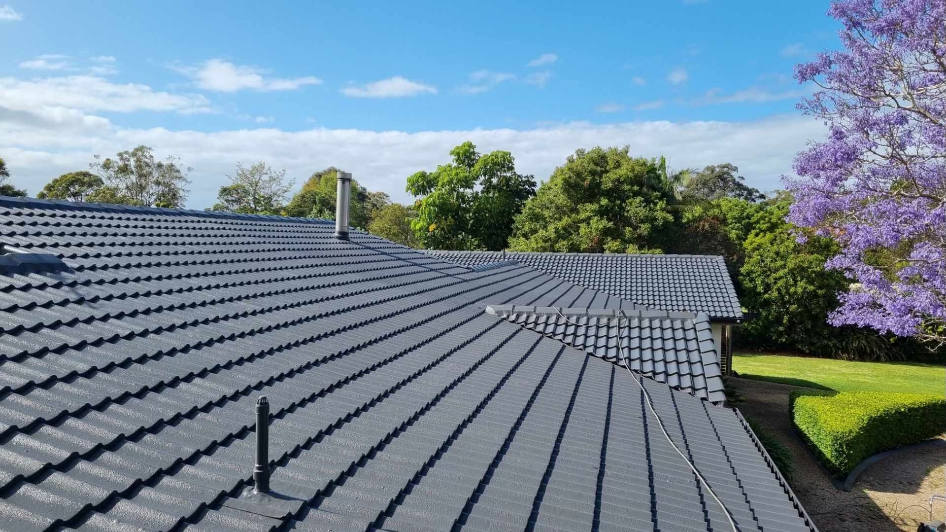 A Roof Of A House With A Purple Tree In The Background — Rooftech Roofing Services in Iluka, NSW