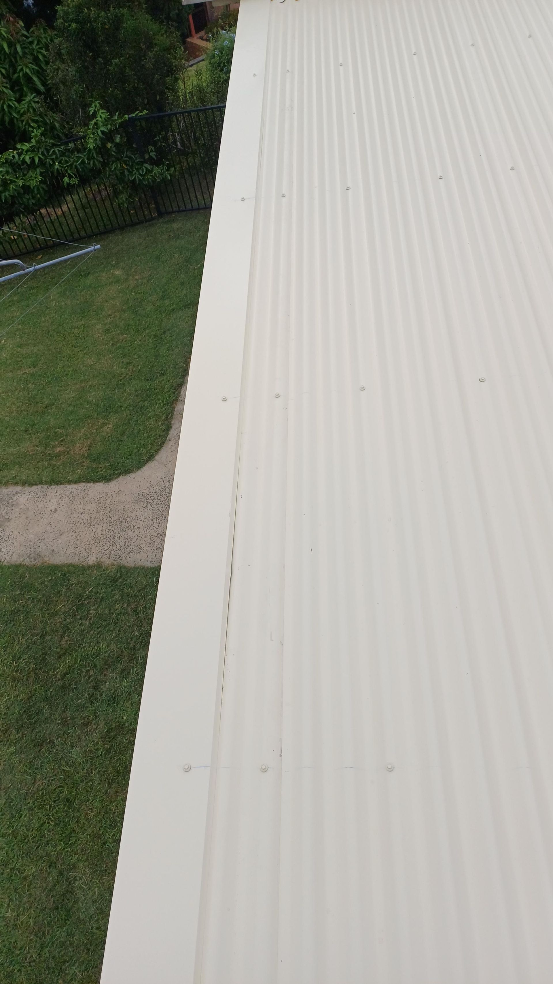 A White Corrugated Metal Roof Is Sitting On Top Of A Lush Green Lawn — Rooftech Roofing Services in Bangalow, NSW