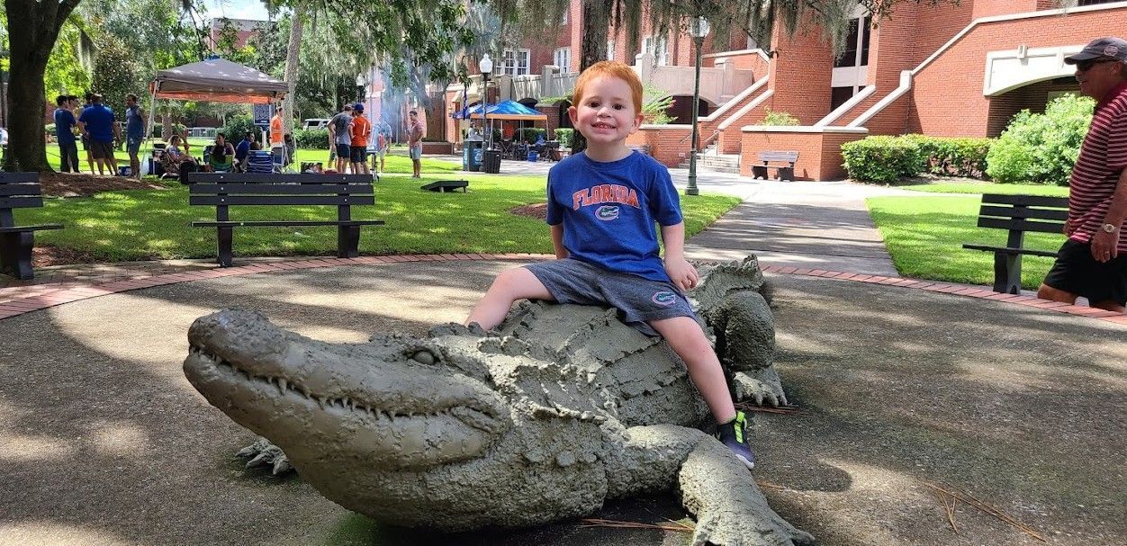 Redheaded boy sitting on a life-like alligataor statue on a brick patio at the University of Florida