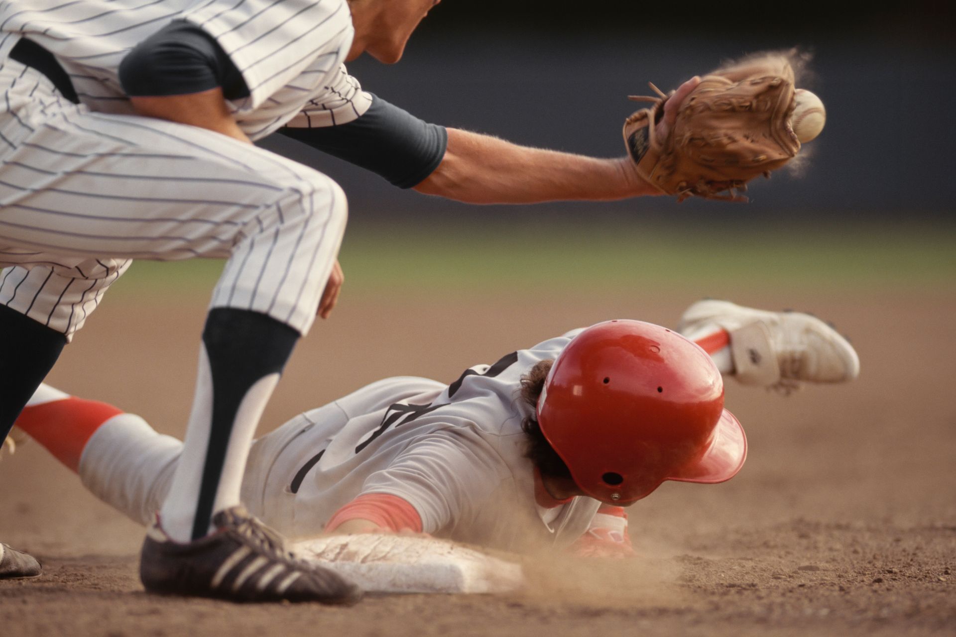 Base runner sliding into base while a fielder catches the ball in a baseball game.