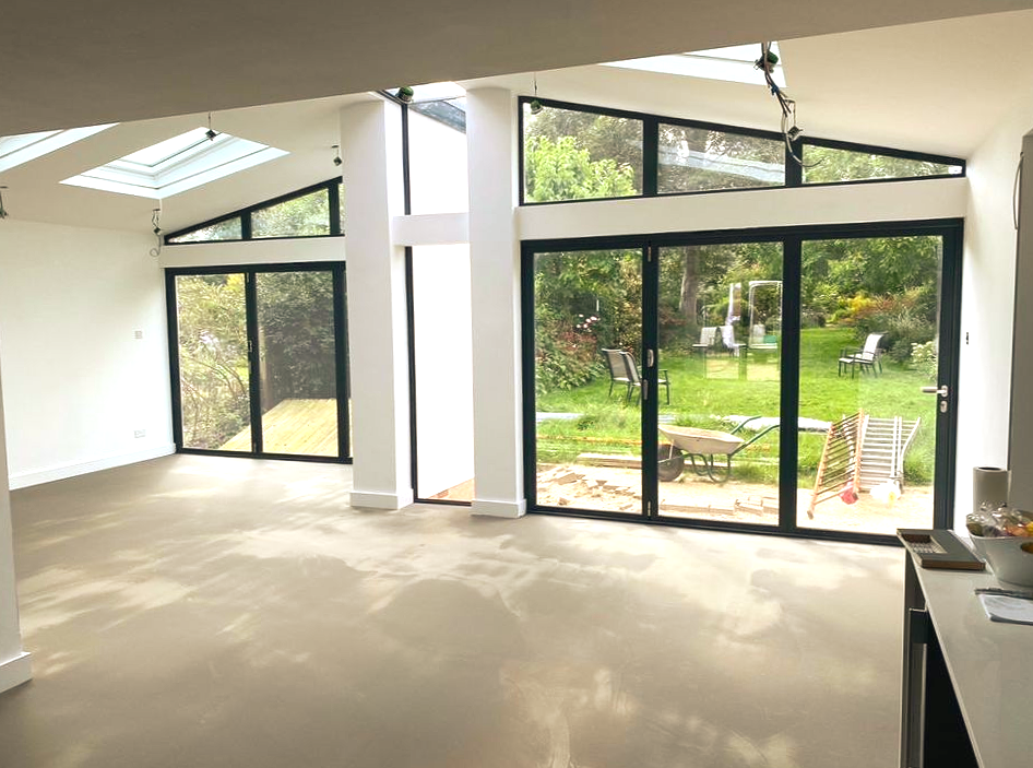 Spacious, bright interior room with large glass doors overlooking a backyard. Sunlight streams in.