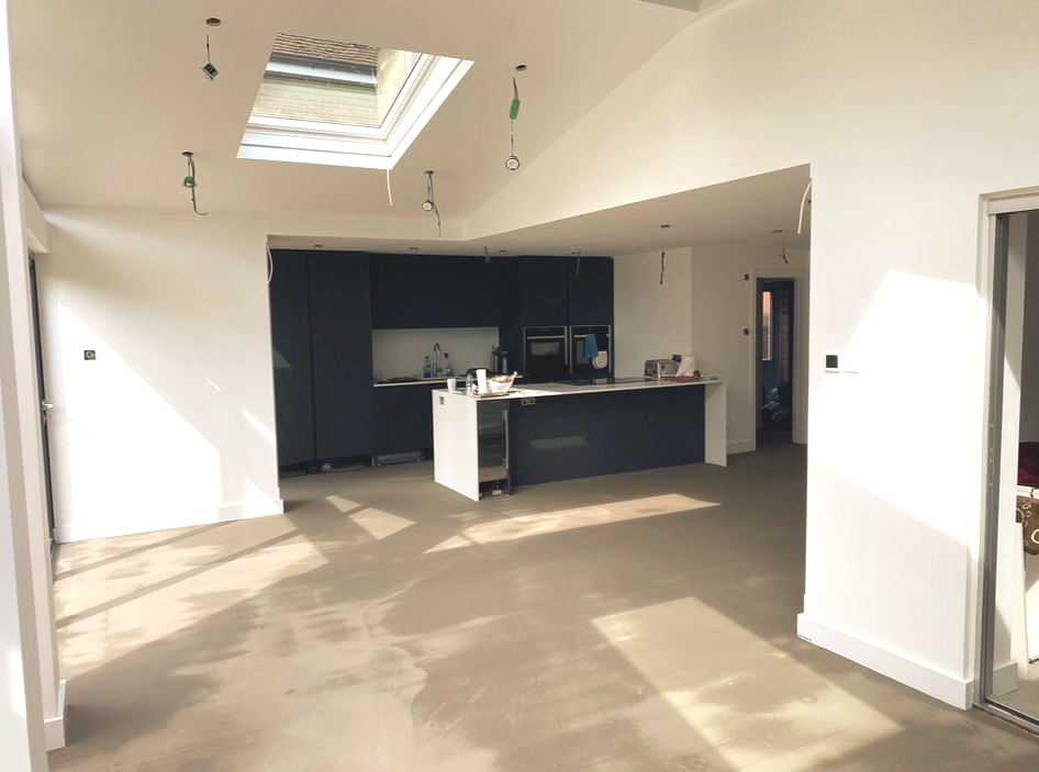 A mostly empty modern kitchen with dark cabinets, skylight, and unfinished flooring.