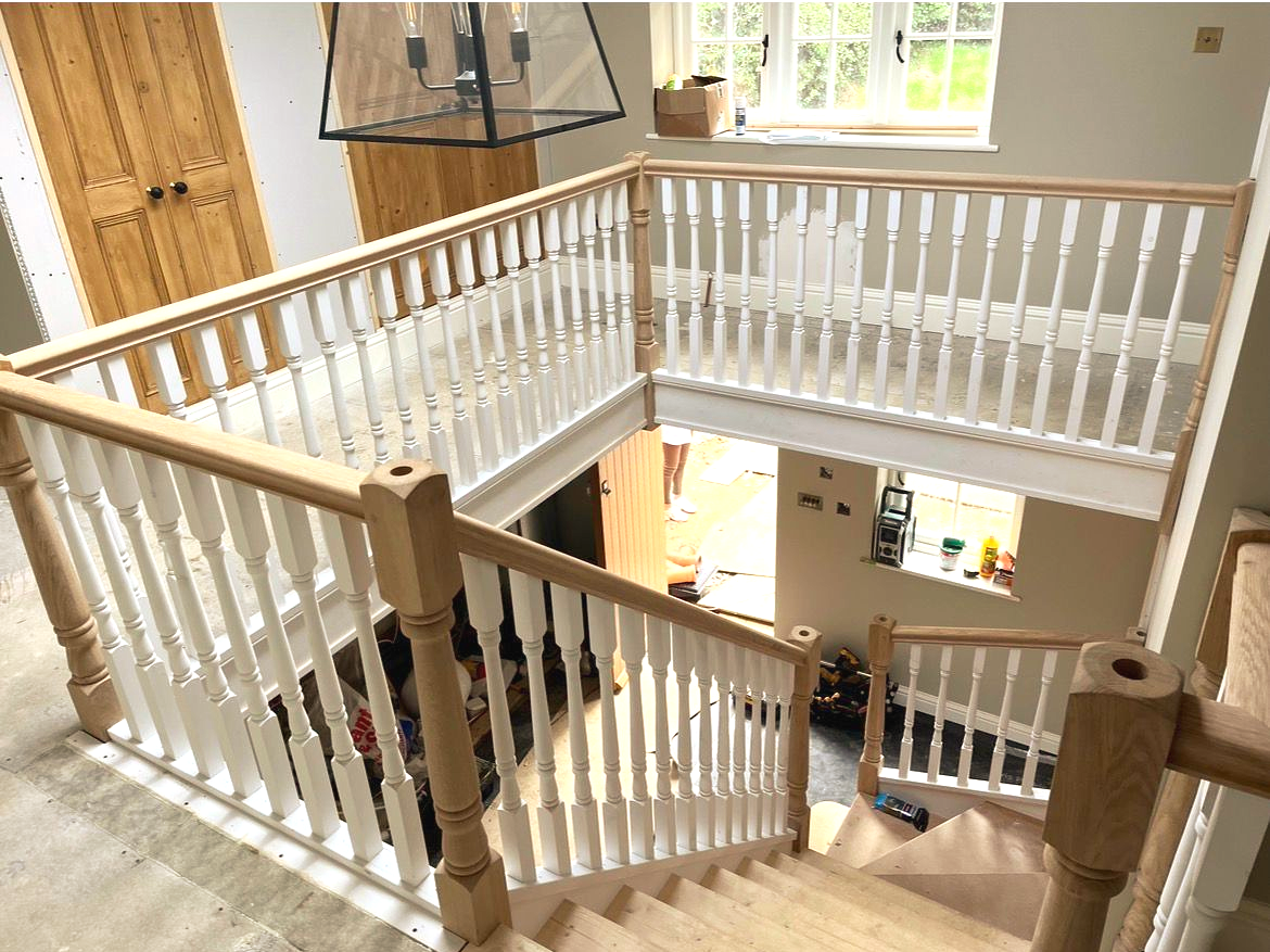 A light-wood staircase with white balusters and a landing, viewed from above.