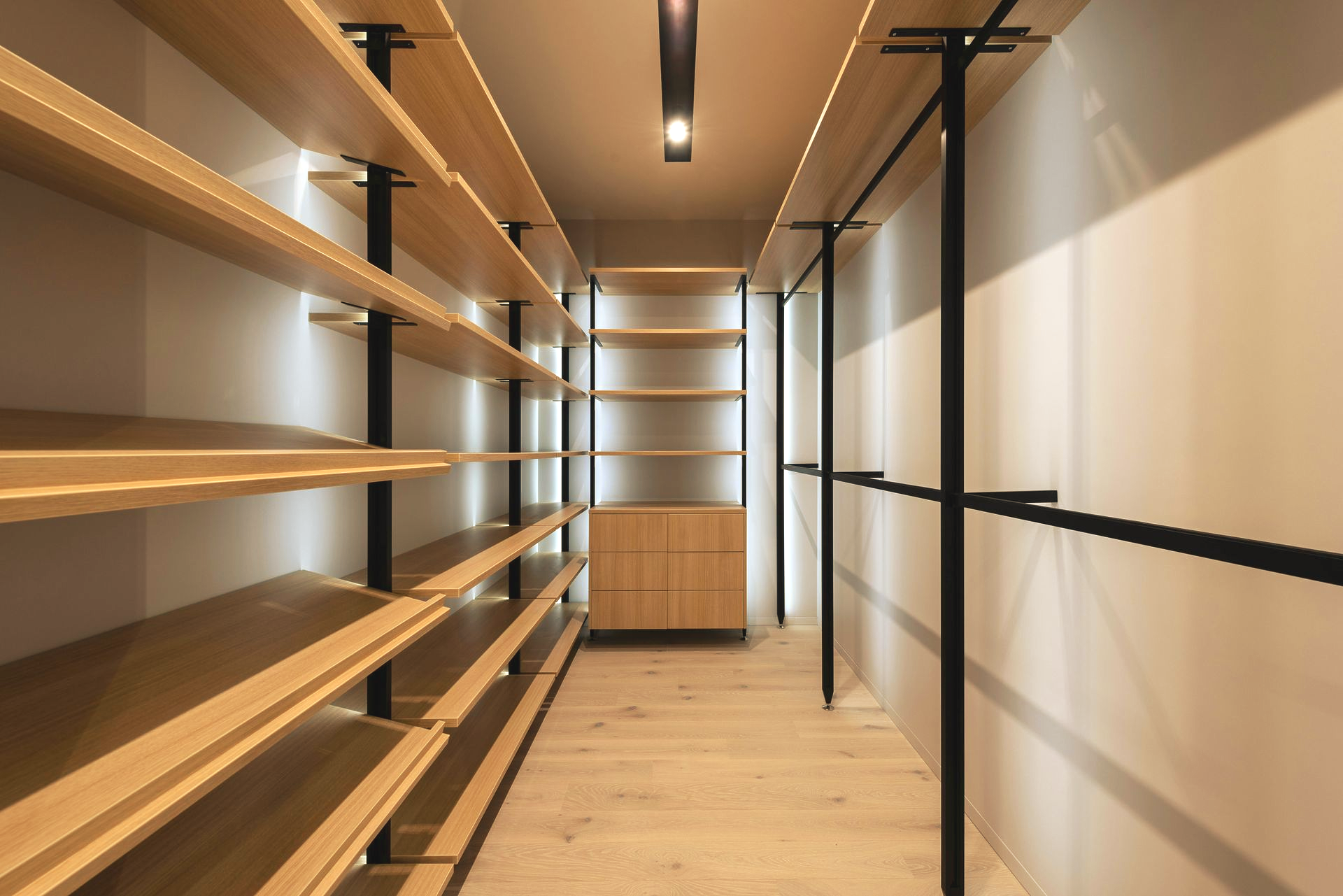Empty, modern walk-in closet with wooden shelves and black metal supports. Soft lighting and wooden floors.
