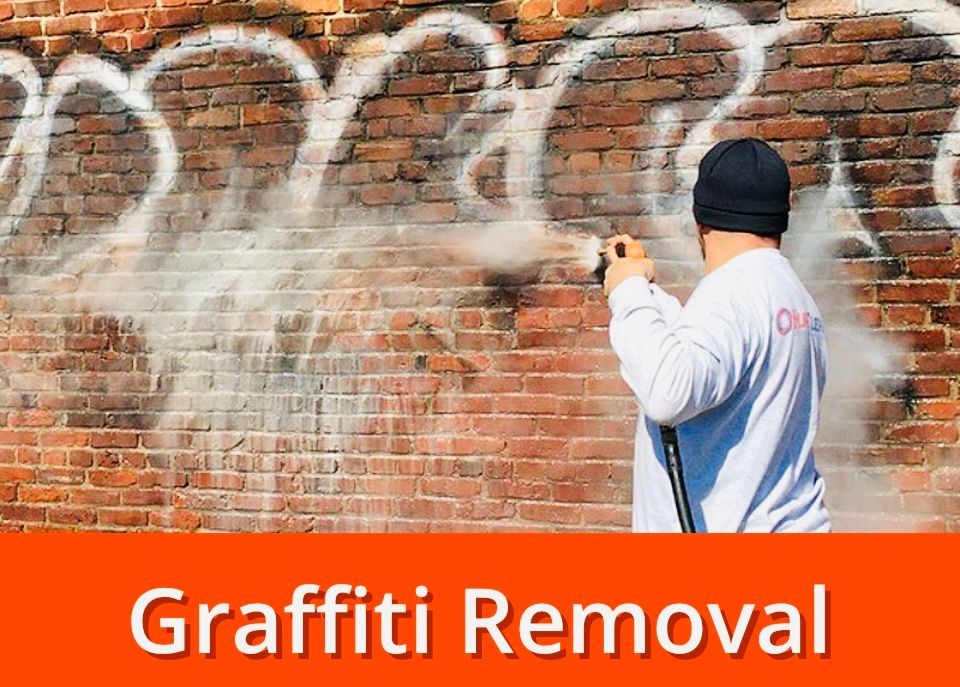 Person power washing graffiti off a brick wall.