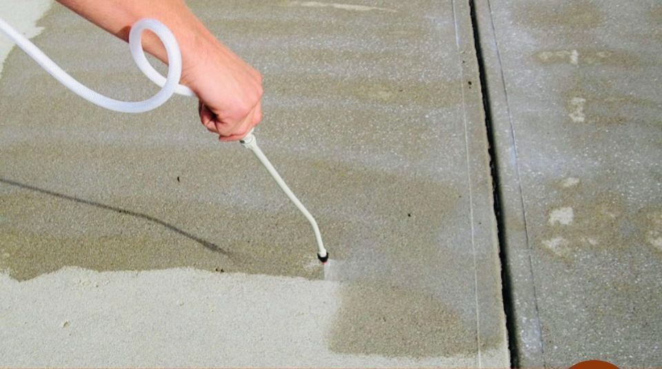 Person spraying concrete with a white hose, cleaning the surface.