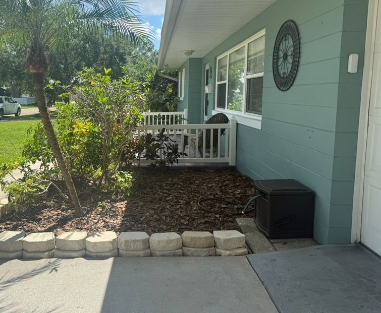 Exterior of a light blue house with a small fenced-in area, mulch, and a black storage box.