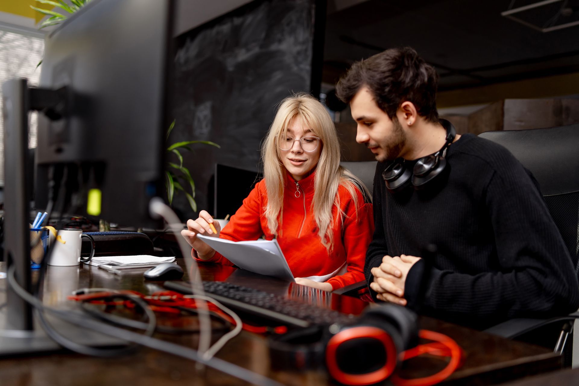 A man and a woman are sitting at a desk looking at a computer screen.