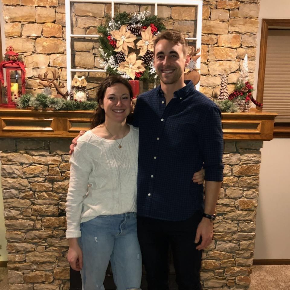 Couple standing in front of a fireplace decorated for the holidays.