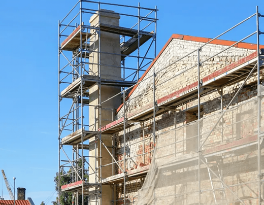 Scaffolding surrounds a building's chimney and wall, indicating ongoing construction or renovation.