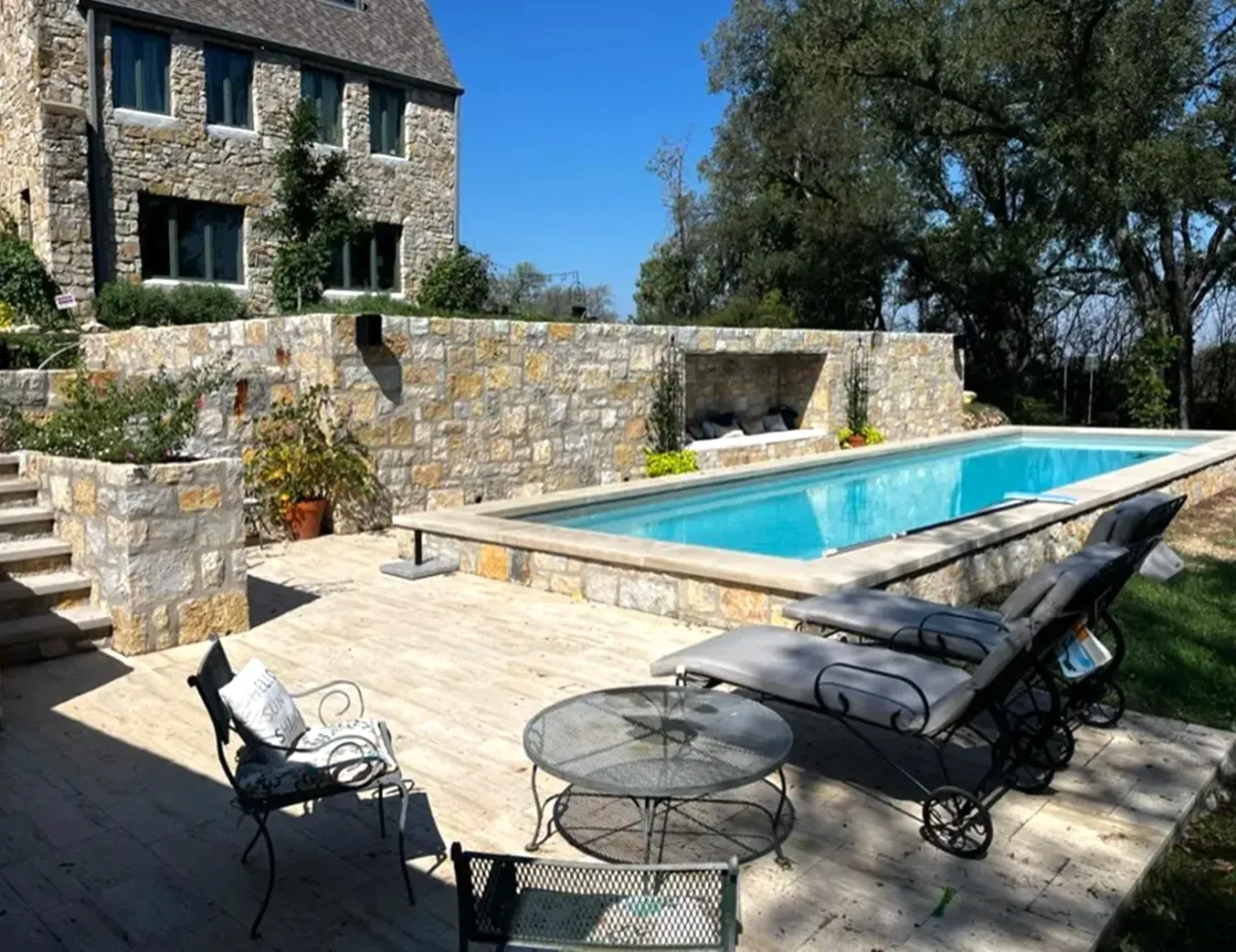 Stone house with a rectangular pool, lounge chairs, and patio furniture.