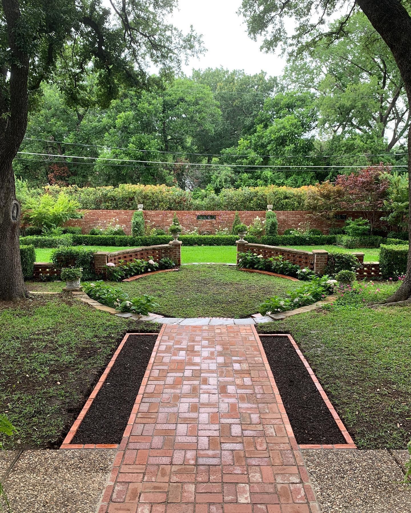 Brick pathway leading to a formal garden with brick walls, hedges, and greenery.