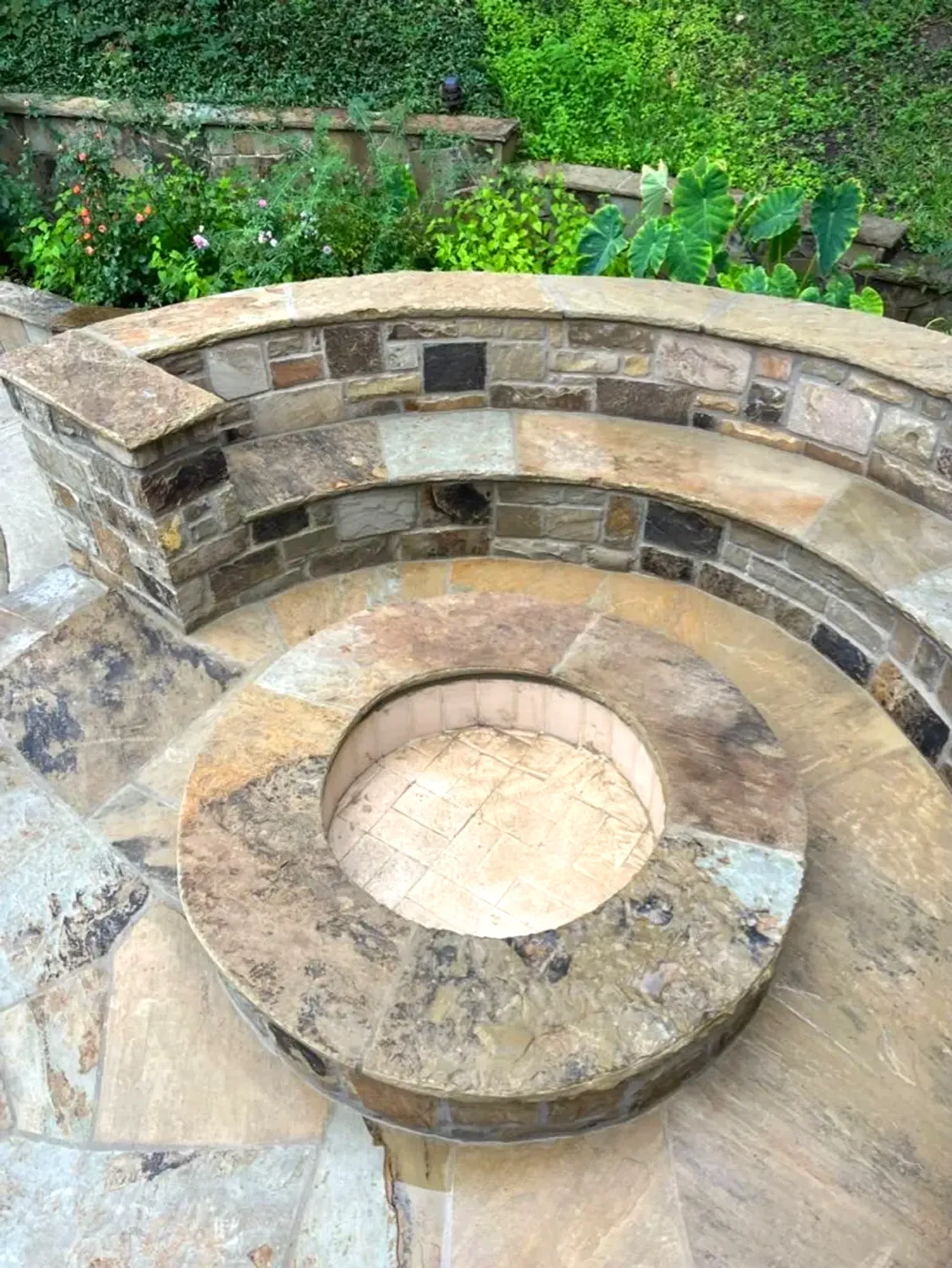 Stone fire pit with surrounding circular seating area, set in a garden.