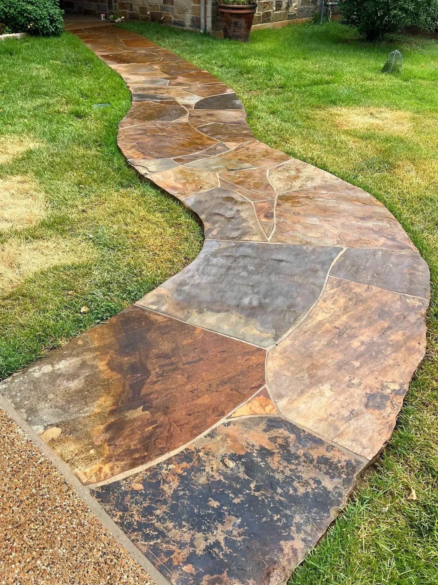 Winding flagstone walkway through green grass, leading toward a house. Stone is multi-colored: brown, gray, and black.