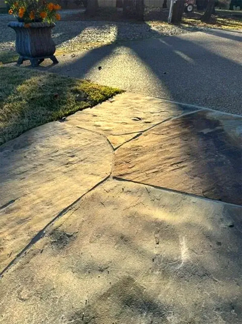 Concrete driveway with decorative pattern; sunlight casts shadows.