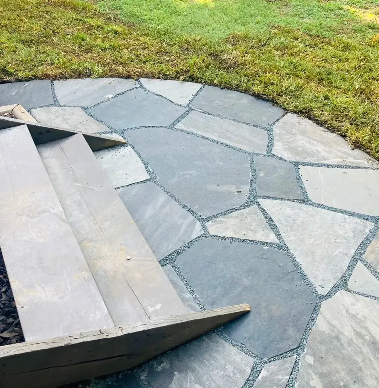 Stone steps leading to a flagstone patio bordered by grass.