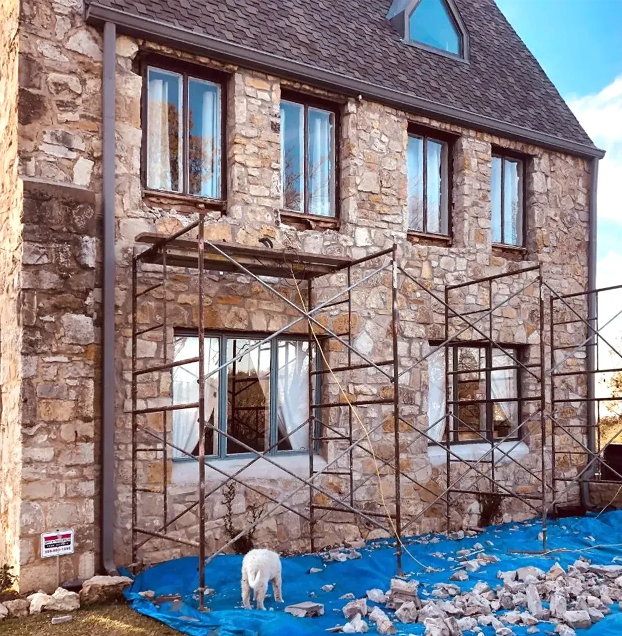 House exterior with scaffolding, stone facade, blue tarp, and dog.