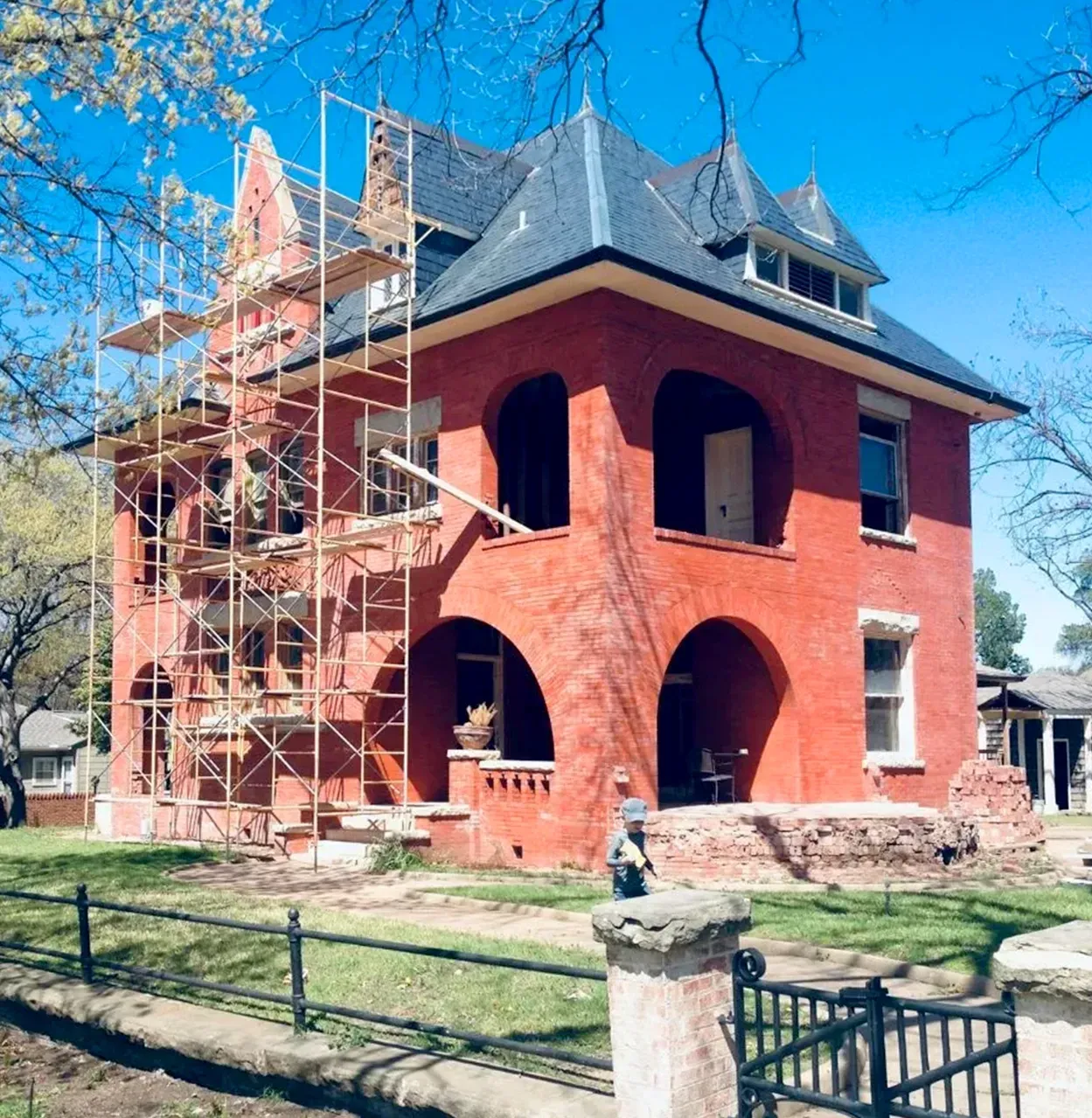 Red brick house under renovation with scaffolding, arched porch, and black roof.