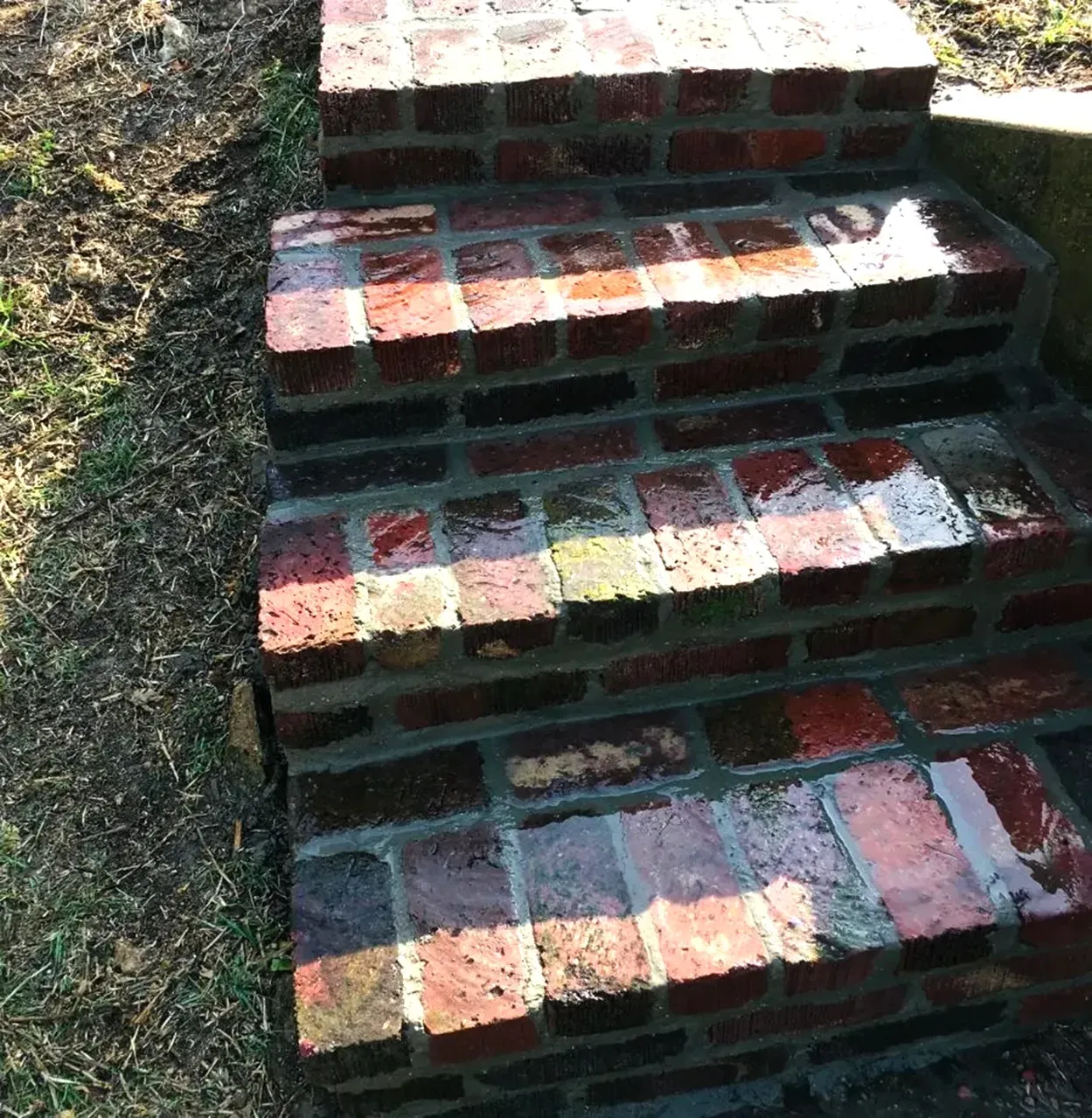 Brick steps leading up. Reddish-brown bricks, wet from rain. Grass and dirt alongside steps.