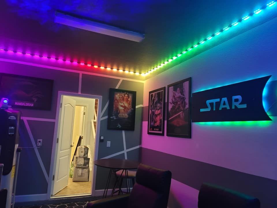 Room with colorful LED lights along ceiling and walls, movie posters, and seating.