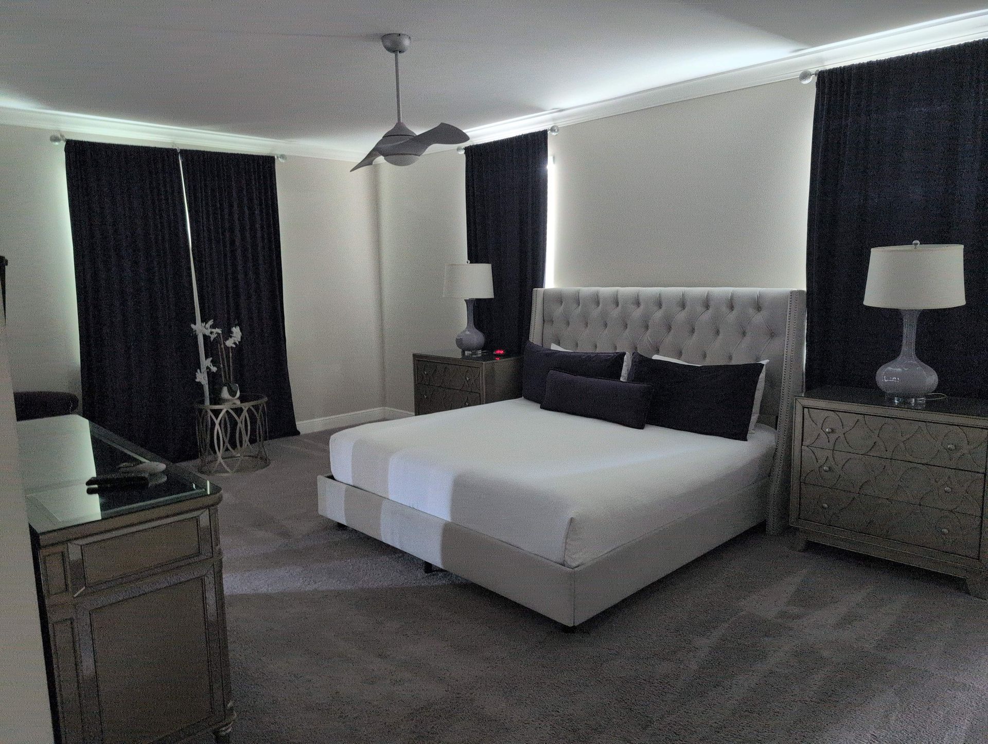 Bedroom with a gray bed, white bedding, black curtains, and matching furniture.
