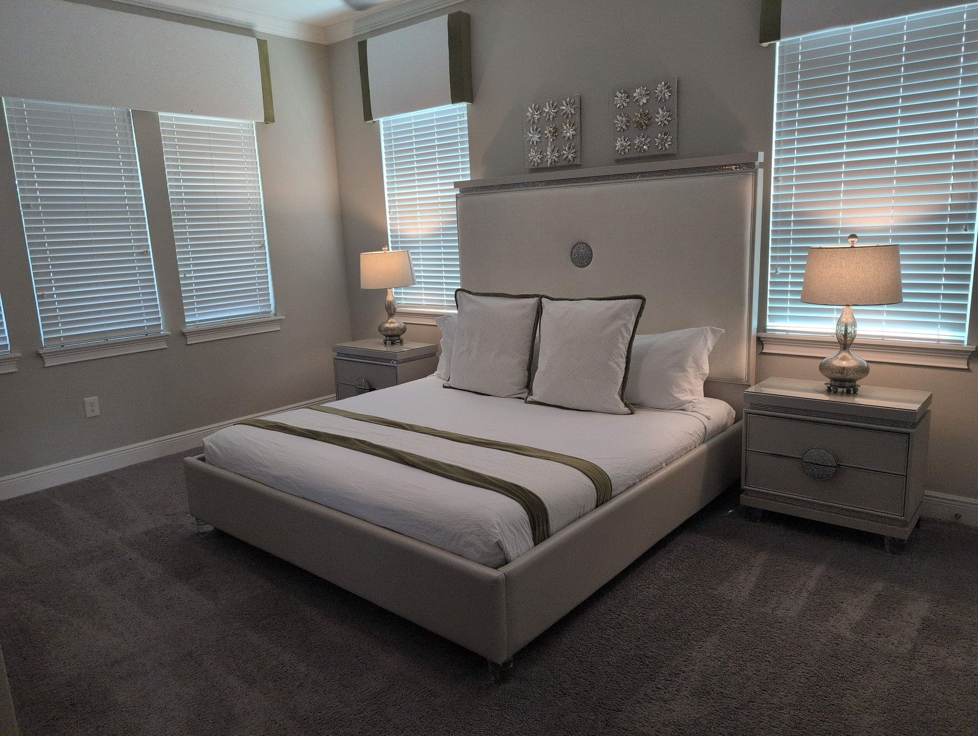 Bedroom with a bed, bedside tables, and windows with blinds. Neutral colors and soft lighting.