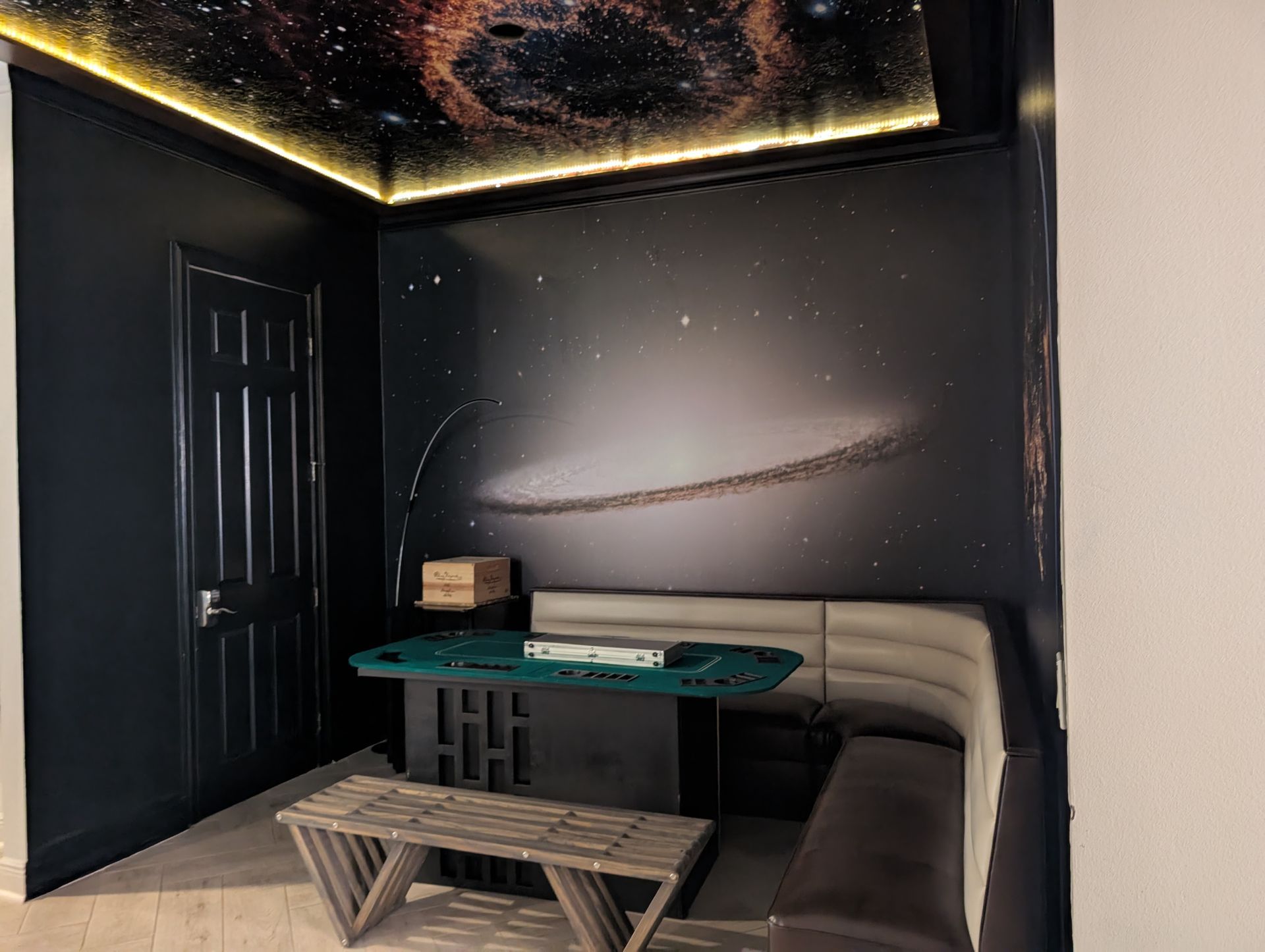 A gaming room with galaxy-themed walls and ceiling, a poker table, and bench seating.