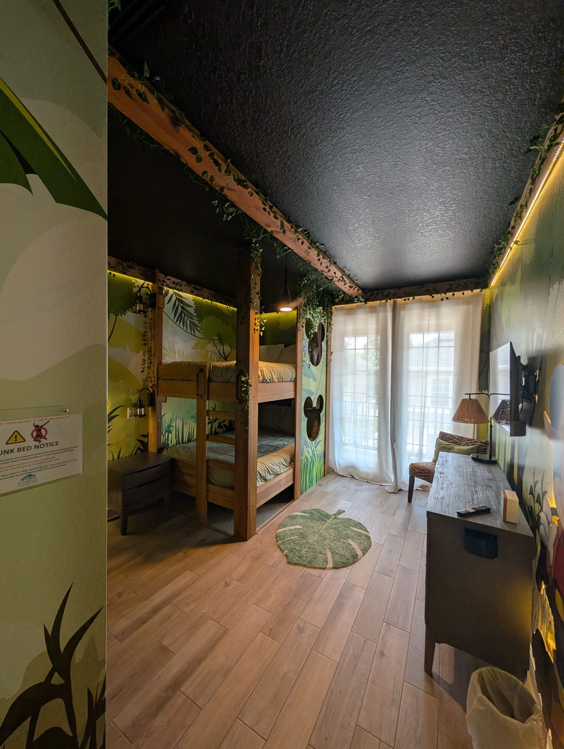 Jungle-themed bedroom with bunk beds, greenery, and a dresser. Green, wood, and white.