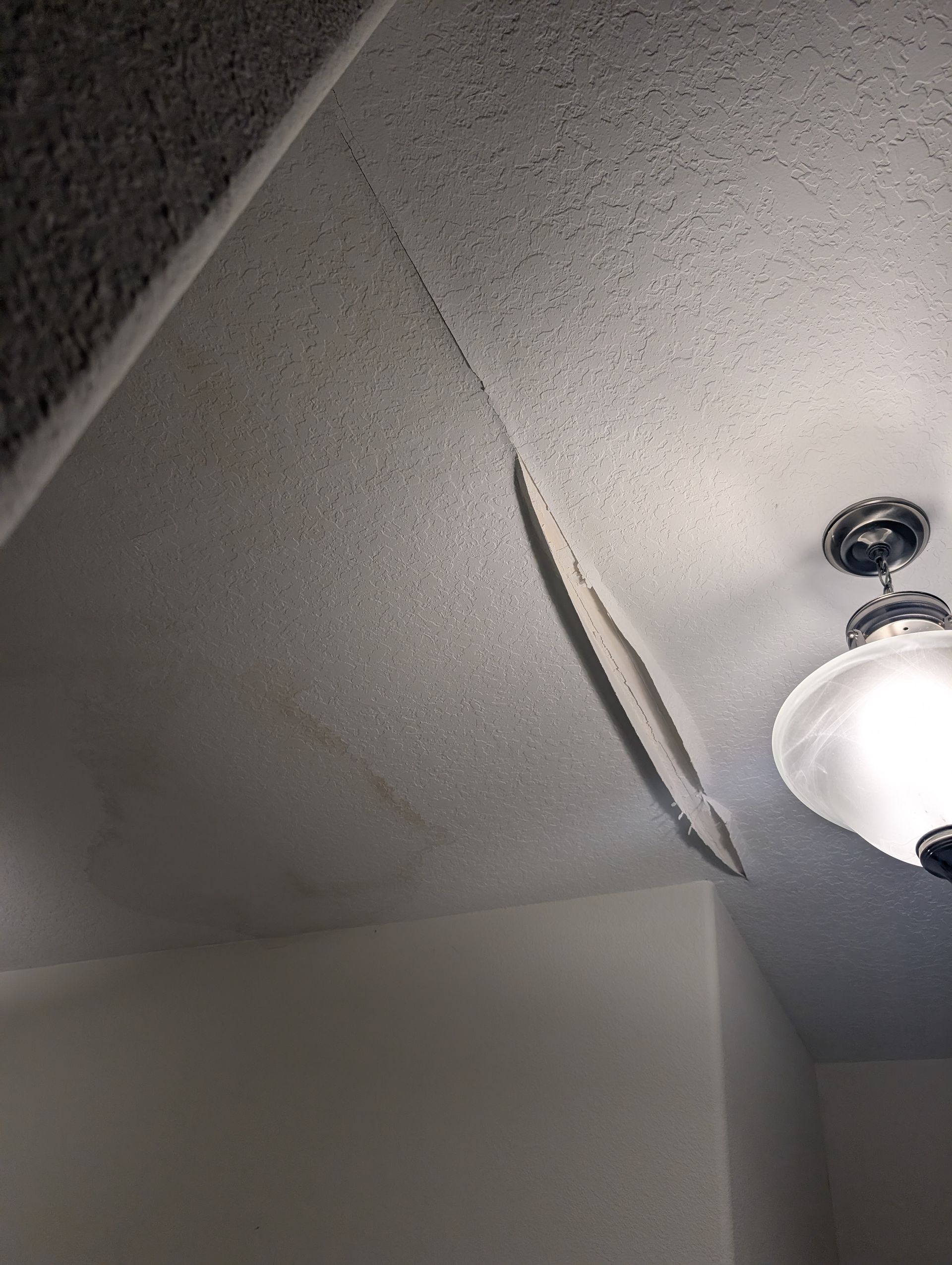 Damaged ceiling in a room with textured finish, peeling and discolored, with a light fixture visible.