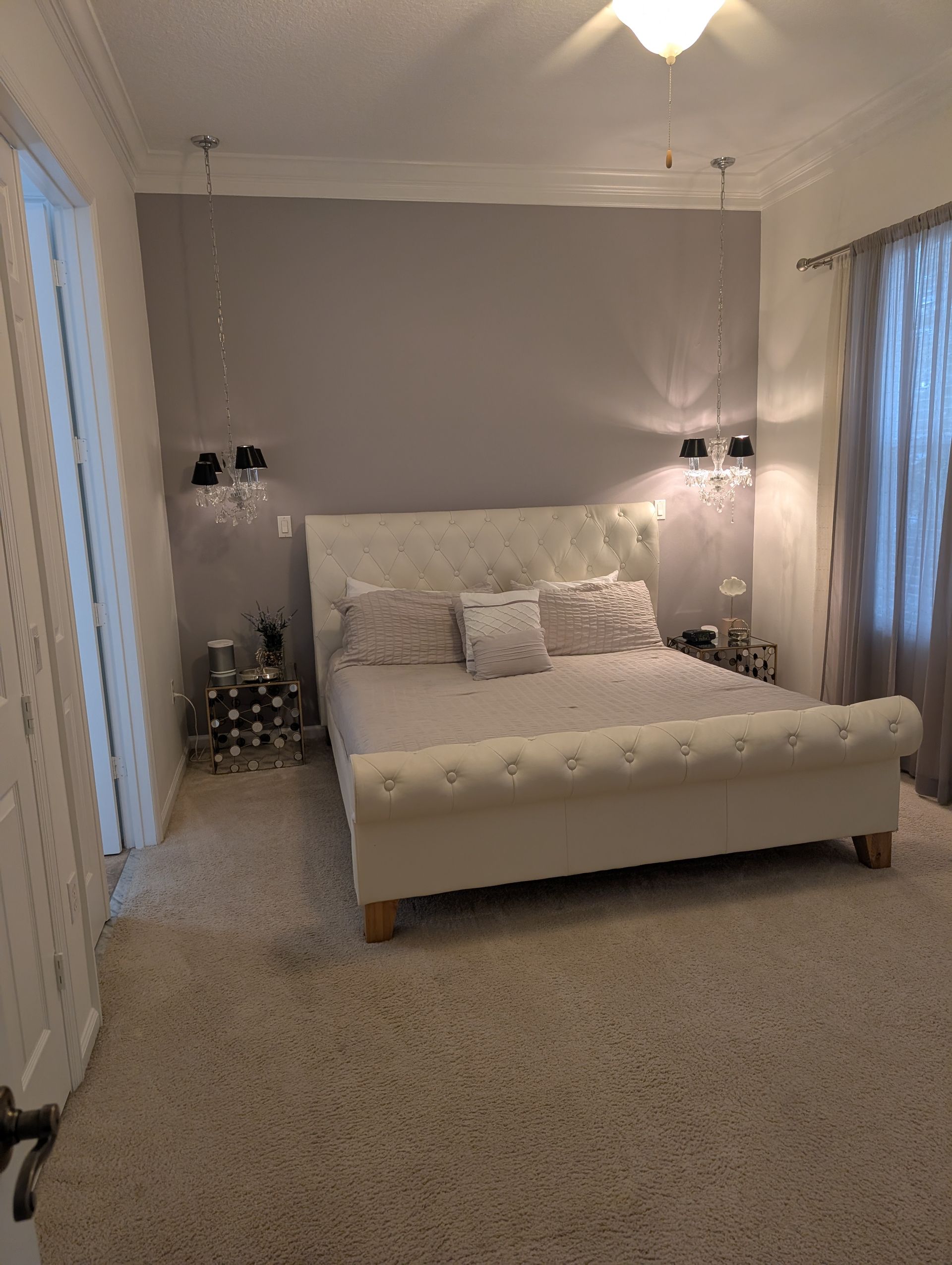 A white bed with a tufted headboard in a gray-walled bedroom with sconces and a fluffy carpet.