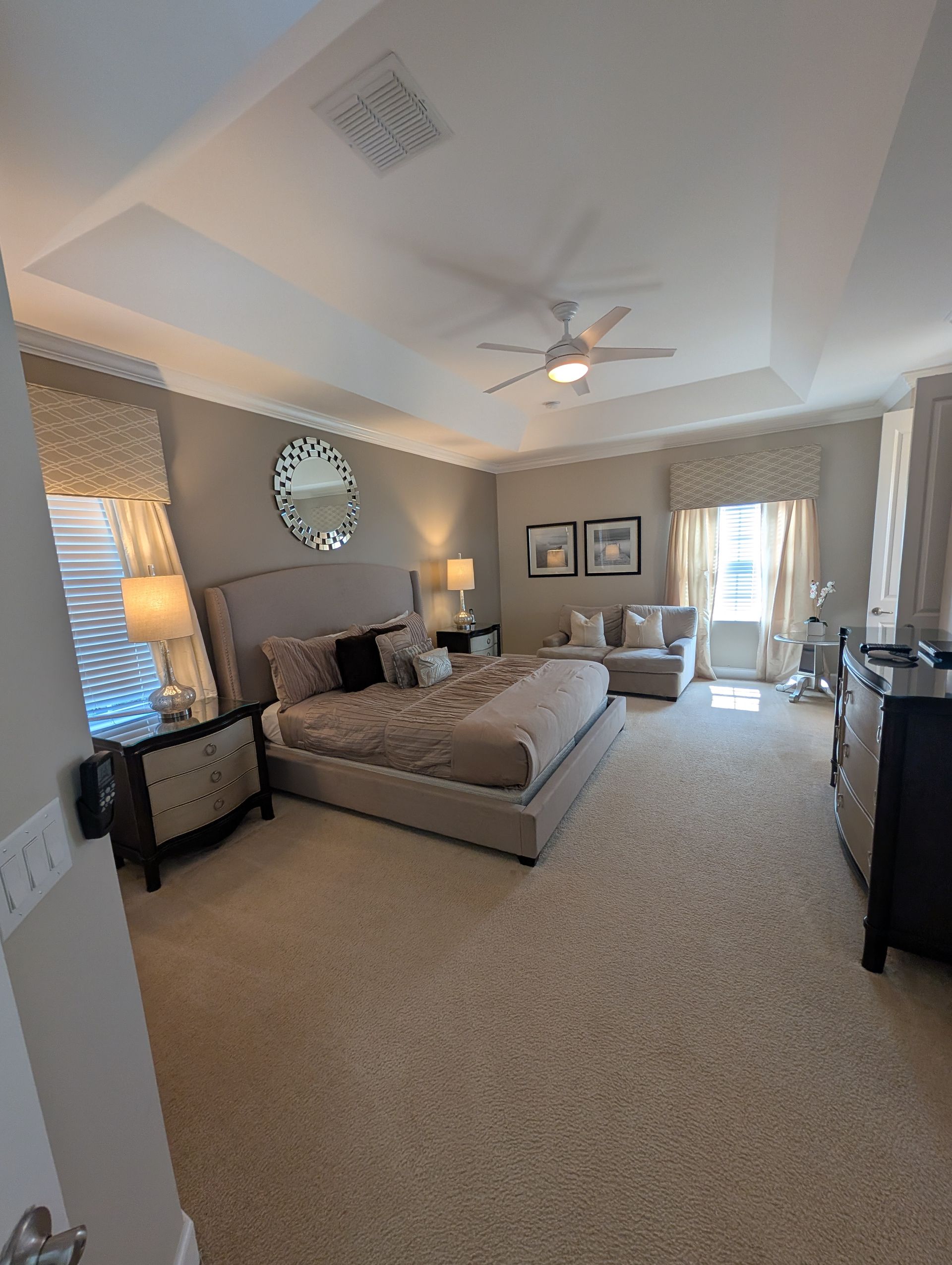 Spacious bedroom with a large bed, neutral colors, sitting area, and a ceiling fan.